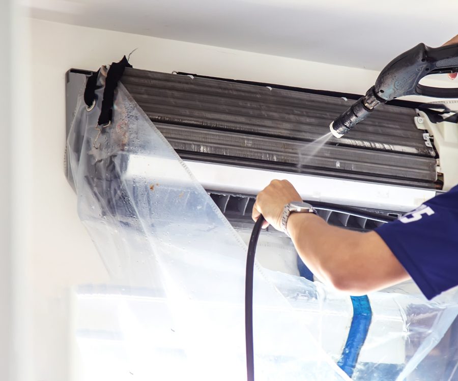 The technicians are cleaning the air conditioner by spraying water. Hand and water spray are cleaning the air conditioner on white background.